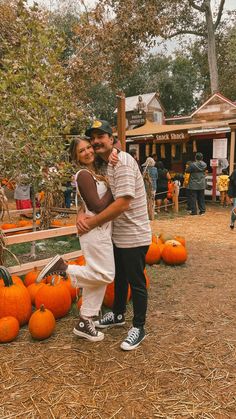 a man and woman standing next to each other in front of pumpkins on the ground