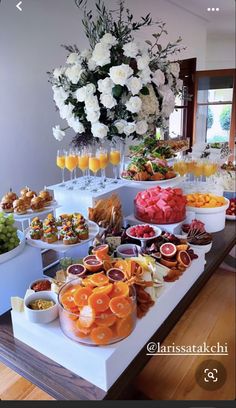 an assortment of fruits and snacks on a buffet table with flowers in the background at a wedding reception