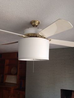 a white ceiling fan hanging from the ceiling in a living room with brick wall and fireplace