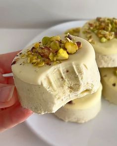 someone is holding some kind of dessert on a white plate with pistachios