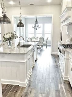 a large kitchen with white cabinets and wood flooring is pictured in this image, there are two chandeliers hanging from the ceiling