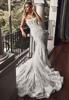 a woman in a white wedding dress standing on a balcony looking at the camera and holding her hand up to her face