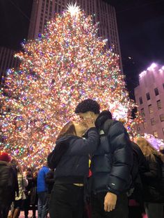 two people standing in front of a large christmas tree