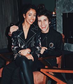 a man and woman sitting next to each other on a wooden chair in front of a fireplace