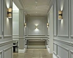 a long hallway with white walls and wooden floors is lit by two lamps on either side of the wall