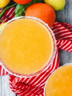 two glasses filled with orange juice sitting on top of a table next to lemons