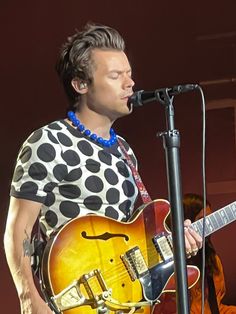 the man is playing his guitar while singing into a microphone and wearing a polka dot shirt