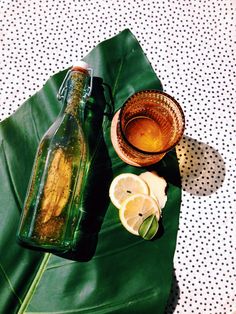 a glass bottle and some lemons on a green banana leaf with a bowl next to it