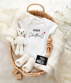 a baby announcement with a teddy bear and other items in a wicker basket on a white blanket