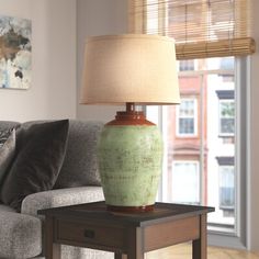 a green vase sitting on top of a wooden table next to a lamp in a living room