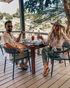 two people sitting at an outdoor table with drinks in front of them, on a deck