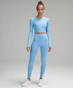 a woman wearing a light blue crop top and matching leggings stands in front of a gray background