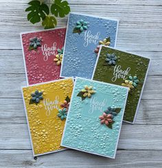 four cards with flowers on them sitting next to a potted plant and some leaves