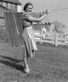 an old black and white photo of a woman hanging out her clothes on a line