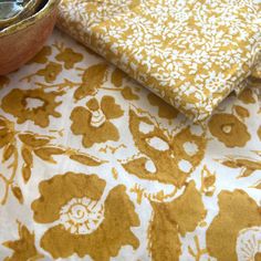 a table topped with yellow and white fabric next to a bowl filled with fruit on top of it