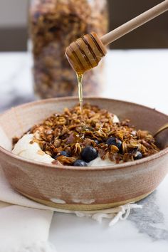 a bowl filled with granola and honey being drizzled on top of it