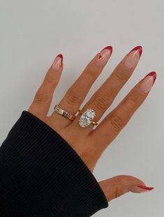 a woman's hand with red fingernails and two rings on her fingers, one ring has an oval diamond in the middle