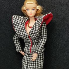 a barbie doll wearing a black and white checkered dress with red collared neckline