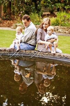 a man, woman and child are sitting on the edge of a pond with their reflection in the water