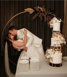 a bride and groom kissing in front of a wedding cake on a table with plates