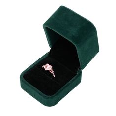 an open green velvet ring box with a pink diamond in it's center, on a white background