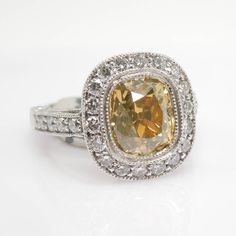 A luscious, natural, sunshine-filled, GIA-certified 2.14 carat Old Mine Cut Fancy Yellow diamond is set in a double mil-grained bezel and surrounded by a halo of 1.20 ct worth of F-G color, VS1-VS2 clarity diamonds. The mounting is made entirely of platinum and this ring would make an excellent engagement ring for the woman who wants something extraordinary. The center stone comes with a GIA certification, and has a clarity of SI2. NB: The color of this stone has proved difficult to photograph a Yellow Diamond Cut Platinum Ring, Yellow Platinum Diamond Ring With Diamond Cut, Yellow Platinum Diamond Ring With Halo Setting, Gia Certified Yellow Diamond Round Ring, Gia Certified Yellow Diamond Ring, Classic Yellow Moissanite Jewelry, Heirloom Yellow Diamond Jewelry, Heirloom Yellow Diamond Ring With Round Shape, Classic Yellow Gia Certified Jewelry