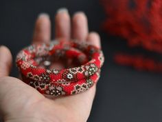 a hand holding a red beaded bracelet on it's wrist and ring in the other hand