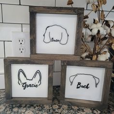 three wooden frames with black and white artwork on them, one has a dog's head