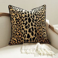 a leopard print pillow sitting on top of a white chair next to a throw pillow