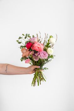 a person's hand holding a bouquet of flowers on a white background with greenery