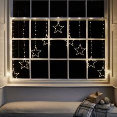 a window that has some lights on it in front of a bed with pillows and blankets