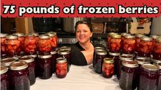 a woman sitting in front of a table full of jars filled with jelly and strawberries