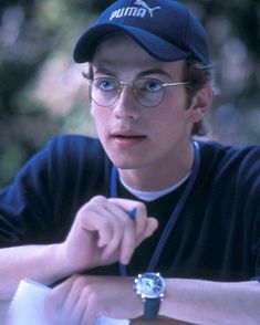 a young man wearing glasses and a hat sitting at a table with a watch on his wrist