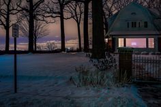 the house is lit up at night in the snowy woods with snow on the ground