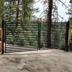 an iron fence with wooden posts in the middle of a dirt area surrounded by trees