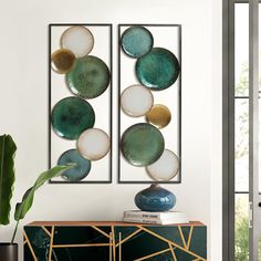 two green and white art pieces hanging on a wall next to a plant in a vase