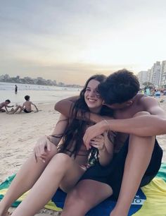 two people sitting on the beach hugging each other