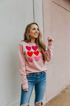 a woman standing against a wall wearing a pink sweater with hearts drawn on the front