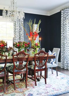 a dining room table with chairs and flowers in vases on the top, next to a chandelier