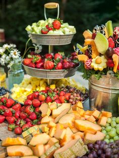 an assortment of fruits and cheeses on display in metal buckets at a buffet table