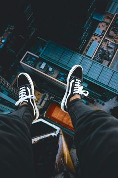 a person standing on top of a building with their feet in the air wearing white and black sneakers