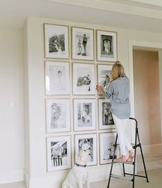 a woman standing on a ladder in front of a wall full of pictures and a dog