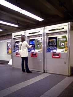 a woman is standing in front of two machines with atms on the sides,