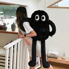 a woman carrying a giant black stuffed animal on her back while walking down the stairs