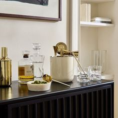 a shelf with bottles and glasses on it next to a wall mounted art piece in the corner