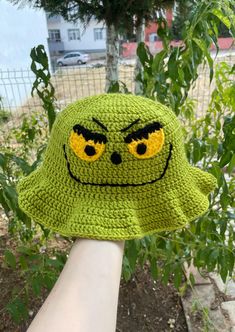 a crocheted green hat with yellow eyes on it's brim is held by a hand