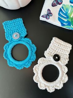 two crocheted items are sitting next to each other on a table, one has a ring and the other has a button