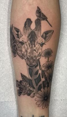 a giraffe with flowers and birds on it's leg is seen in this tattoo