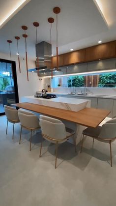 a modern kitchen with an island table surrounded by white chairs and pendant lights hanging from the ceiling