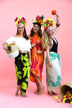 three beautiful women standing next to each other in front of a pink background with fruit on their heads